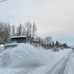 Three large snow plows in a line driving down snowy street