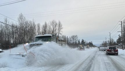 Three large snow plows in a line driving down snowy street