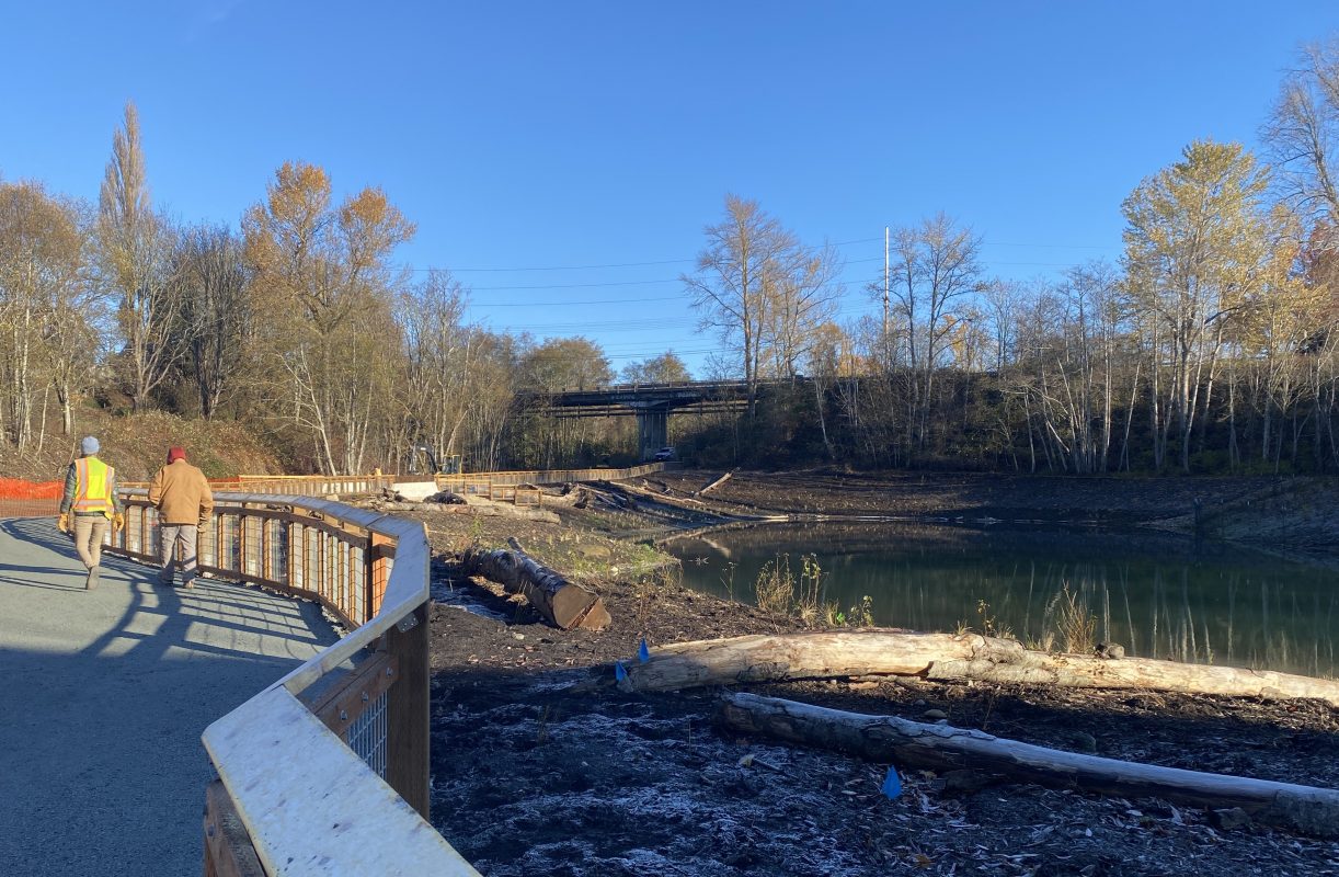 Trail with wooden fence along the side of a waterbody with fall foliage