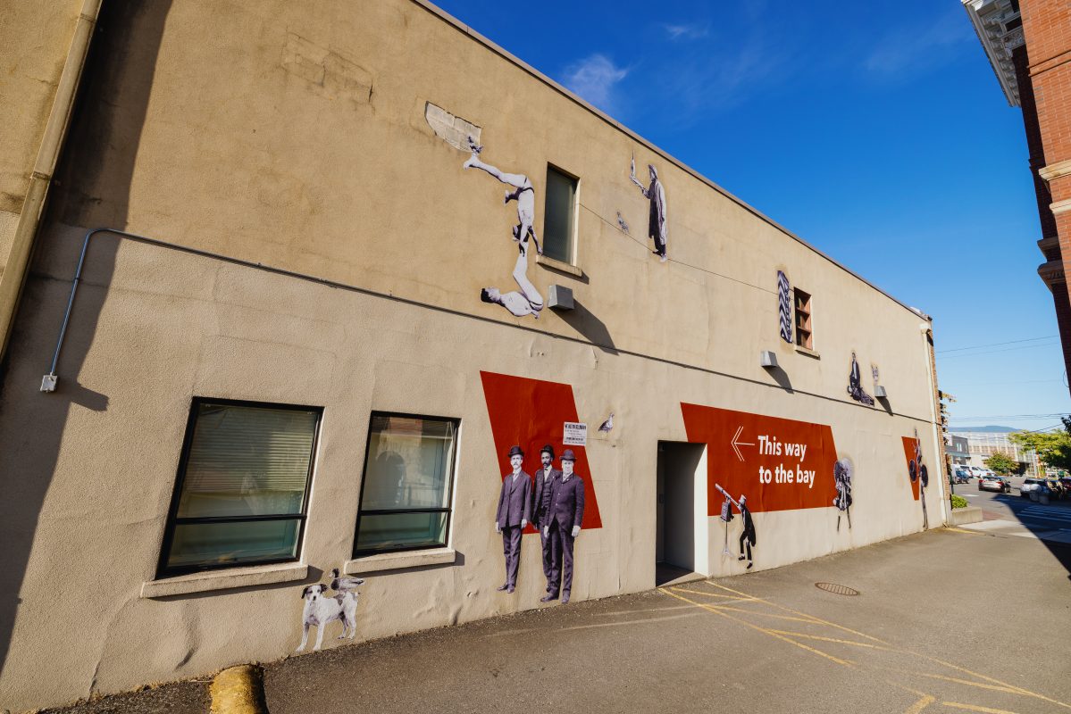 Side of a building showing historical figures from Bellingham and an arrow showing how to get to the bay.