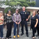 Police officer stands with 5 other adults all smiling at the camera.