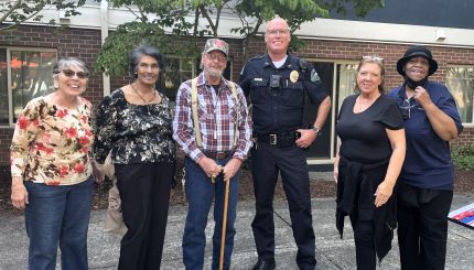 Police officer stands with 5 other adults all smiling at the camera.