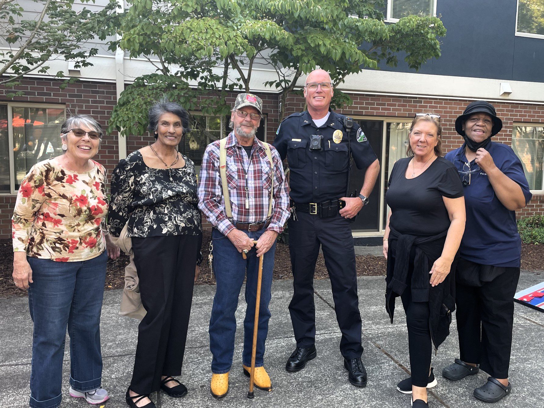 Police officer stands with 5 other adults all smiling at the camera.