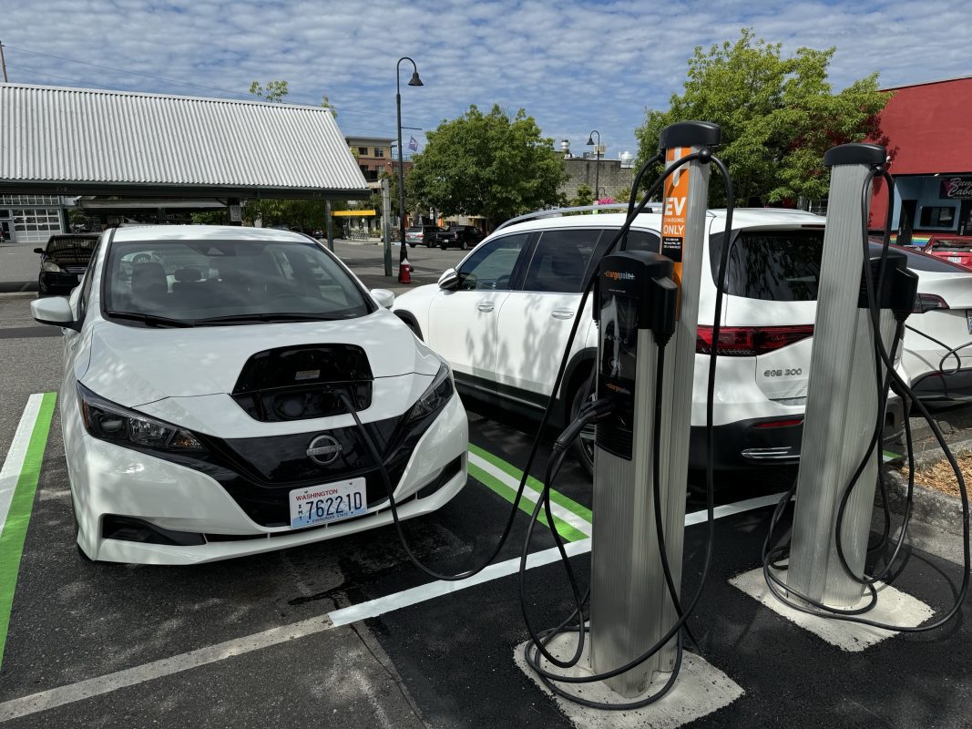 Two electric vehicles are charging at EV stations with Depot Market Square in the background