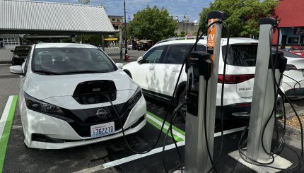 Two electric vehicles are charging at EV stations with Depot Market Square in the background