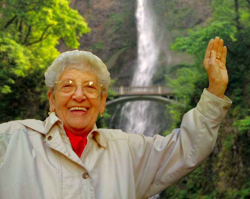 Woman standing in front of waterfall waving and smiling
