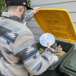 Person adding food scraps to a green bin with yellow lid