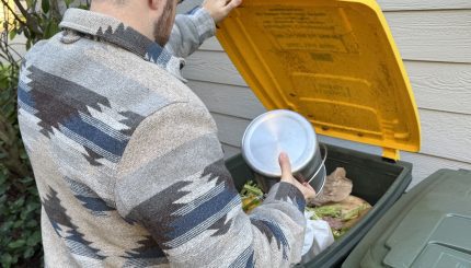 Person adding food scraps to a green bin with yellow lid