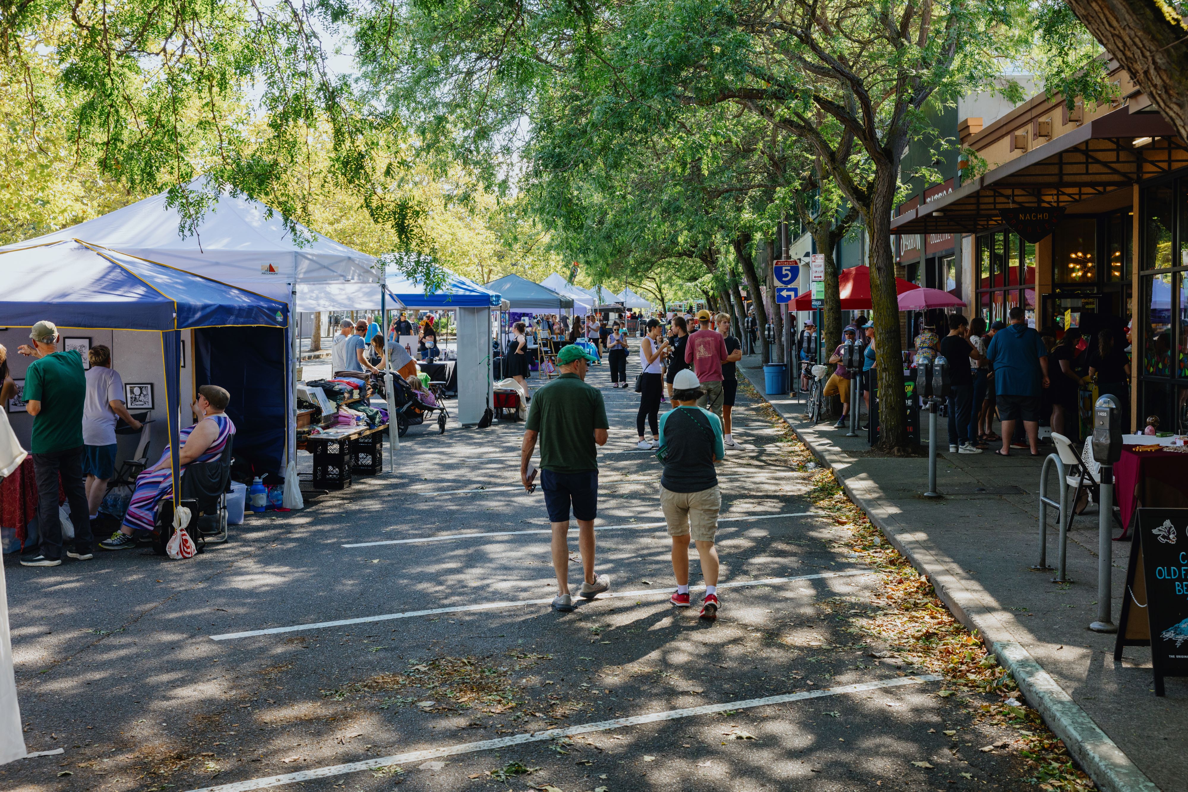 Booths line Railroad Avenue while people walk and shop nearby.