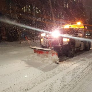 snow plow with head lights driving on snowy street in the dark