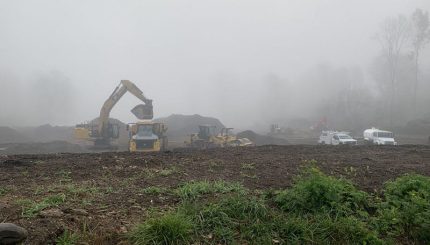 Foggy morning with construction equipment moving dirt in open field