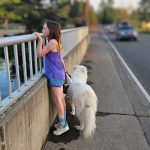 Girl with white dog looking over bridge railing as car approaches