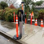 New electric vehicle charging station along road on a rainy day. Orange cone in front of station to block use.
