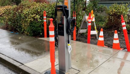 New electric vehicle charging station along road on a rainy day. Orange cone in front of station to block use.