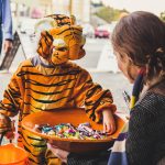 Child in tiger costume choosing candy from a bowl being held by an adult