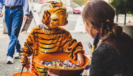 Child in tiger costume choosing candy from a bowl being held by an adult