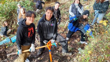 Group of volunteers posing for a photo on a hillside while holding tools.