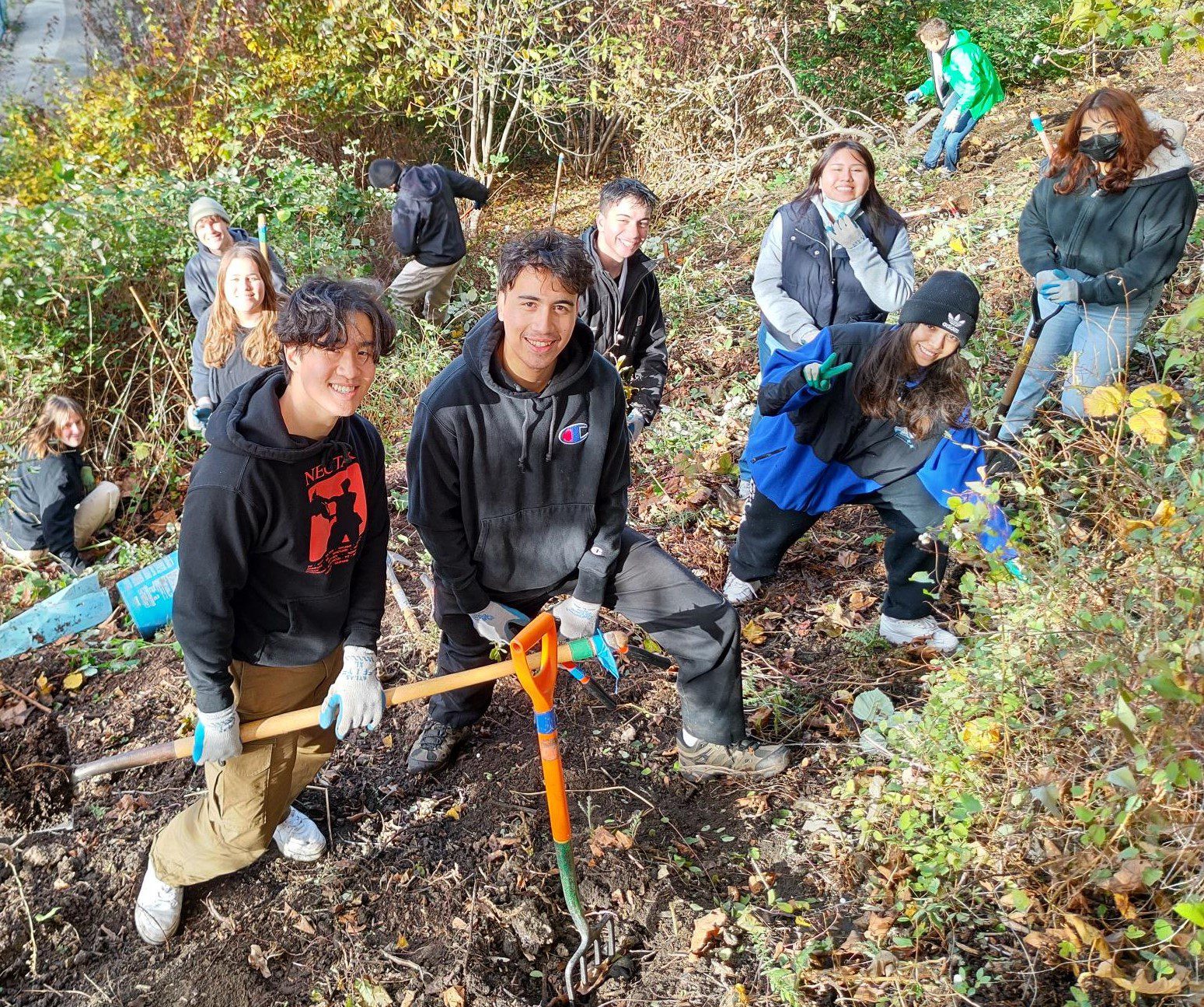 Group of volunteers posing for a photo on a hillside while holding tools.