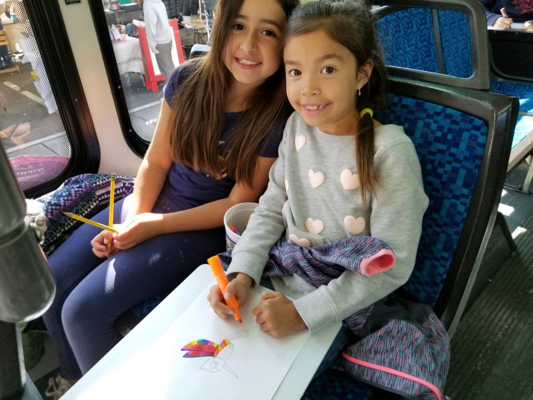 Two children sitting on bus coloring a picture.