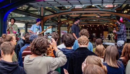 People gathered at a concert looking up at a stage where musicians play.