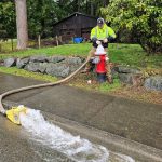man at hydrant as water rushes out hose down the street