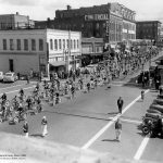 Historic photo of many youth on bicycles riding down street
