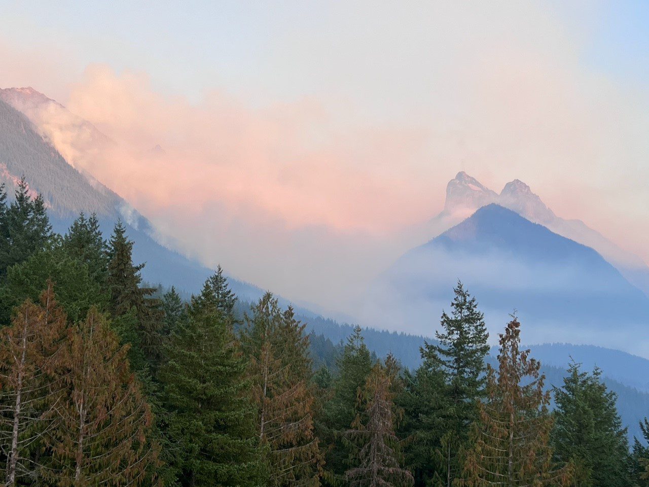 Wildfire smoke in a mountainous, forested area.