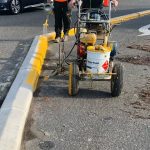 Workers spray yellow paint on roadway curb to increase visibility