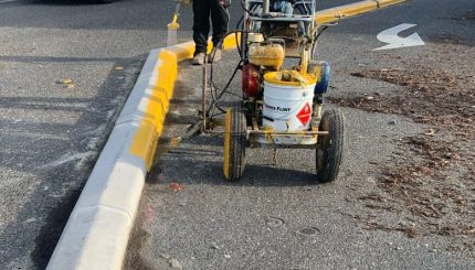 Workers spray yellow paint on roadway curb to increase visibility