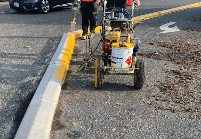 Workers spray yellow paint on roadway curb to increase visibility