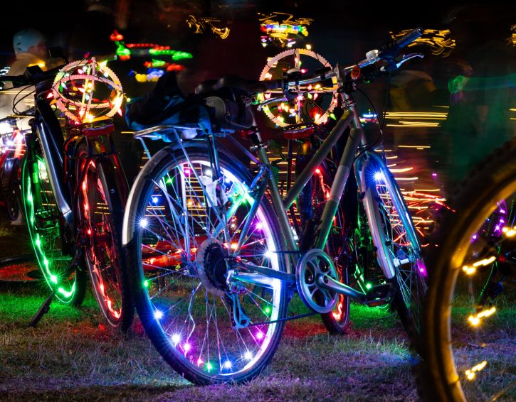 Bicycles lined up in the grass in the dark with colorful lights in the wheels.