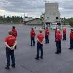 11 people standing in 2 lines in red shirts the say "recruit" on the back