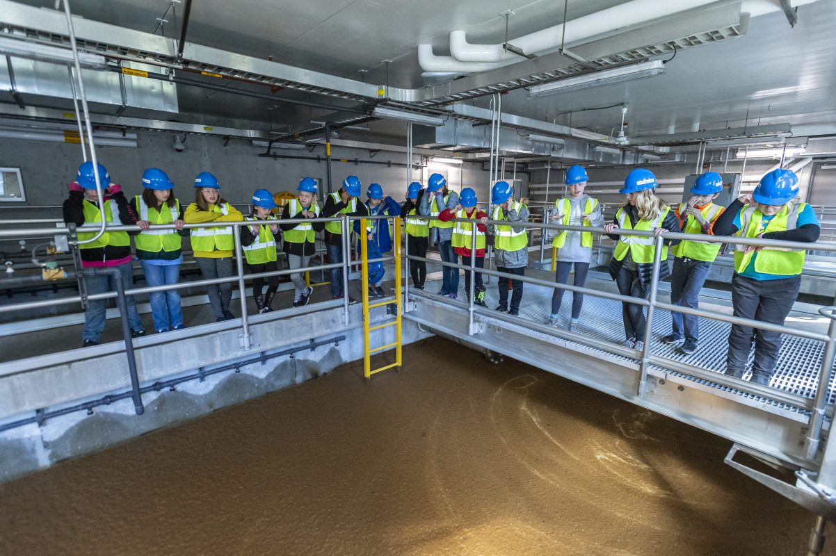 Group of school children in bright yellow vests on a tour looking at a water treatment process.
