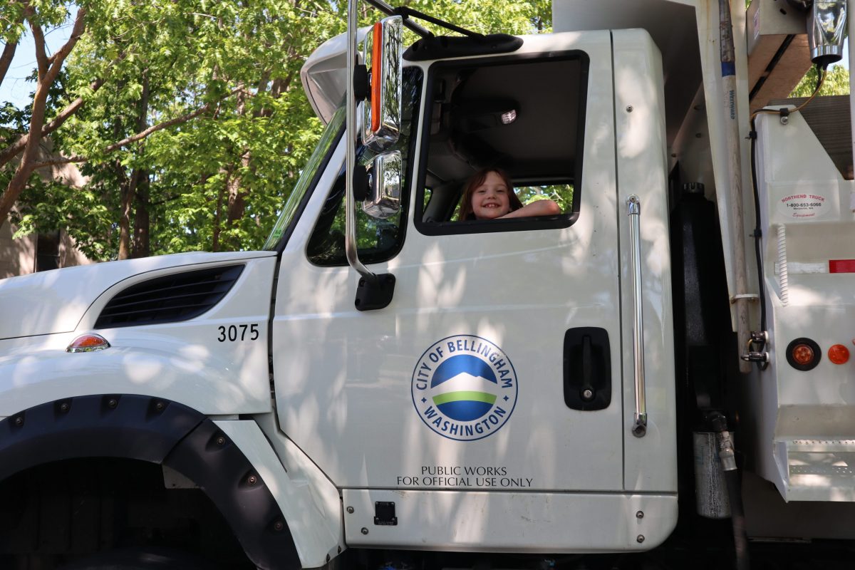 Young girl sitting in parked truck smiling out window. The truck has a City of Bellingham logo on it.