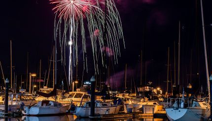 boats docked in harbor at night with bright red firework radiating out and cascading down