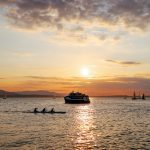 People enjoy Bellingham Bay by ferry, sailboat, and canoe with a sunset in the background