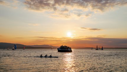 People enjoy Bellingham Bay by ferry, sailboat, and canoe with a sunset in the background