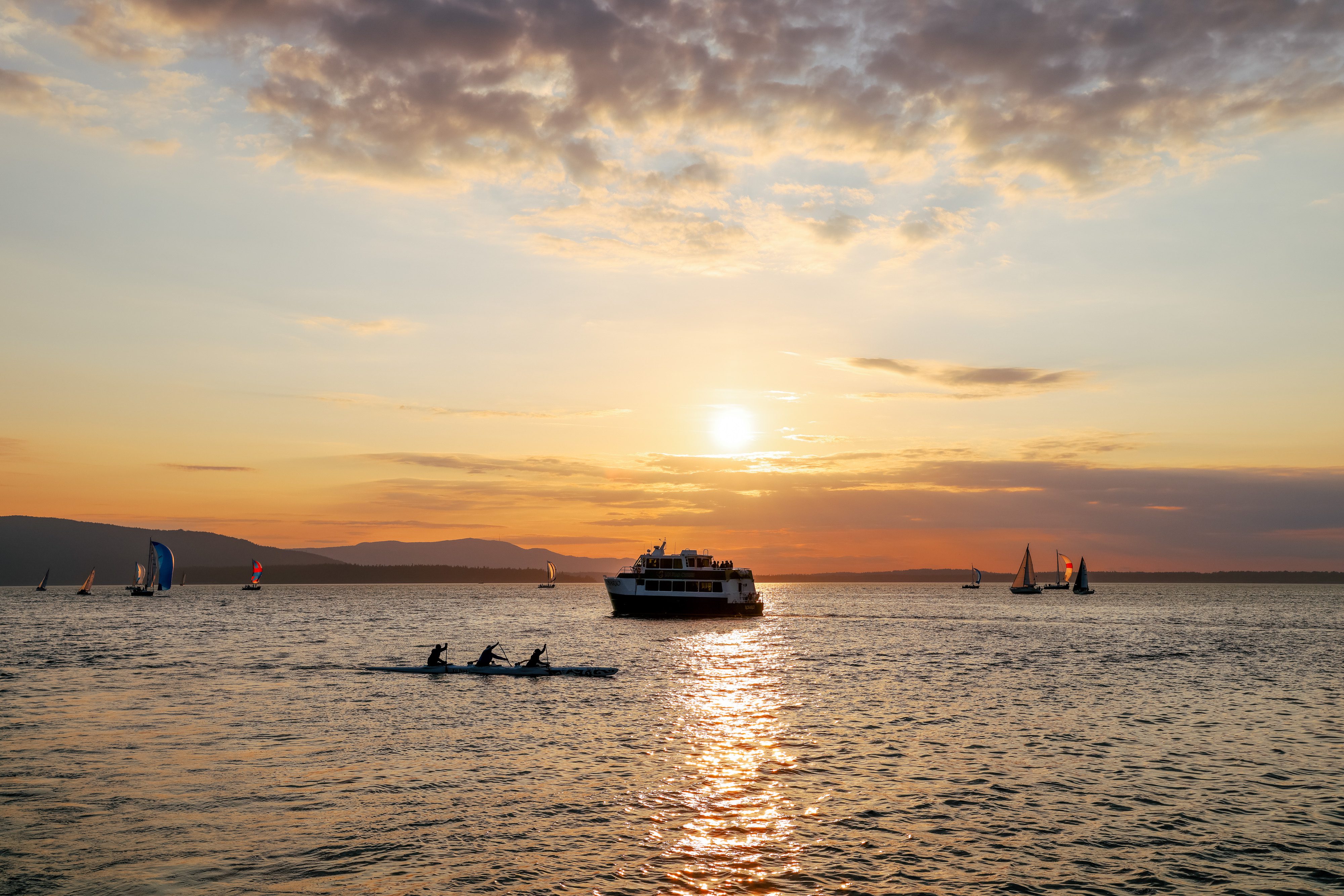 People enjoy Bellingham Bay by ferry, sailboat, and canoe with a sunset in the background