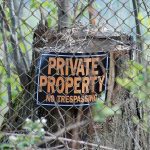 "private property no trespassing" sign on tree stump behind chain link fence