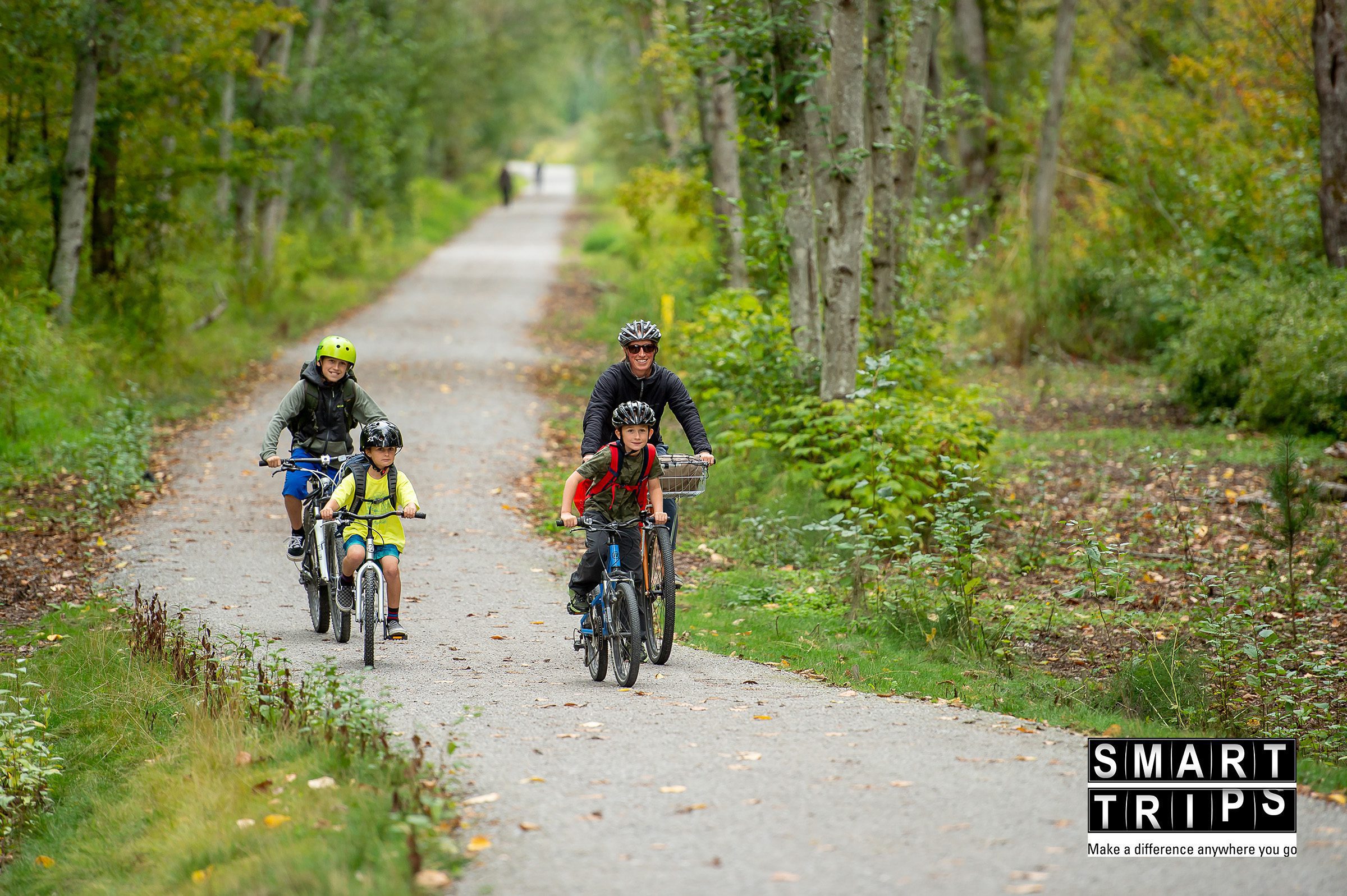 Adult man and three children biking together on a forested trail.