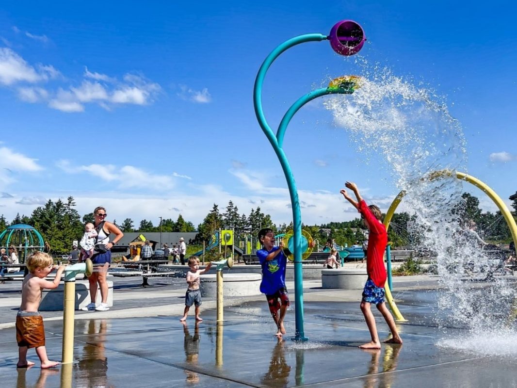 Several children playing in water being strayed from structures in a park on a sunny day