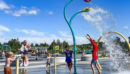 Several children playing in water being strayed from structures in a park on a sunny day