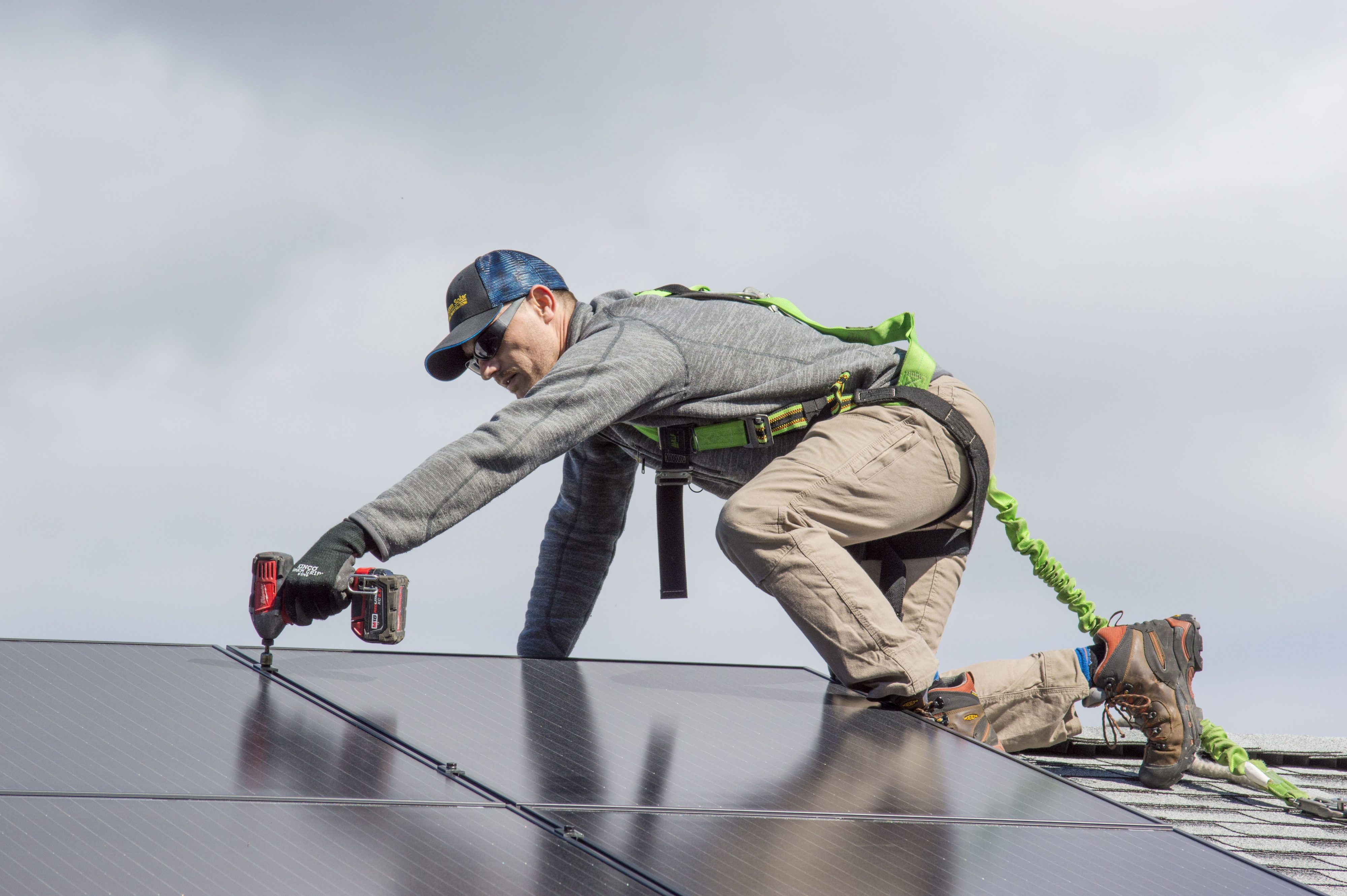 Man on roof of a building using a drill to install solar panels.