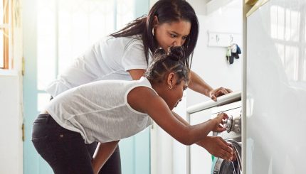 Mother and daughter looking at washing machine together. 